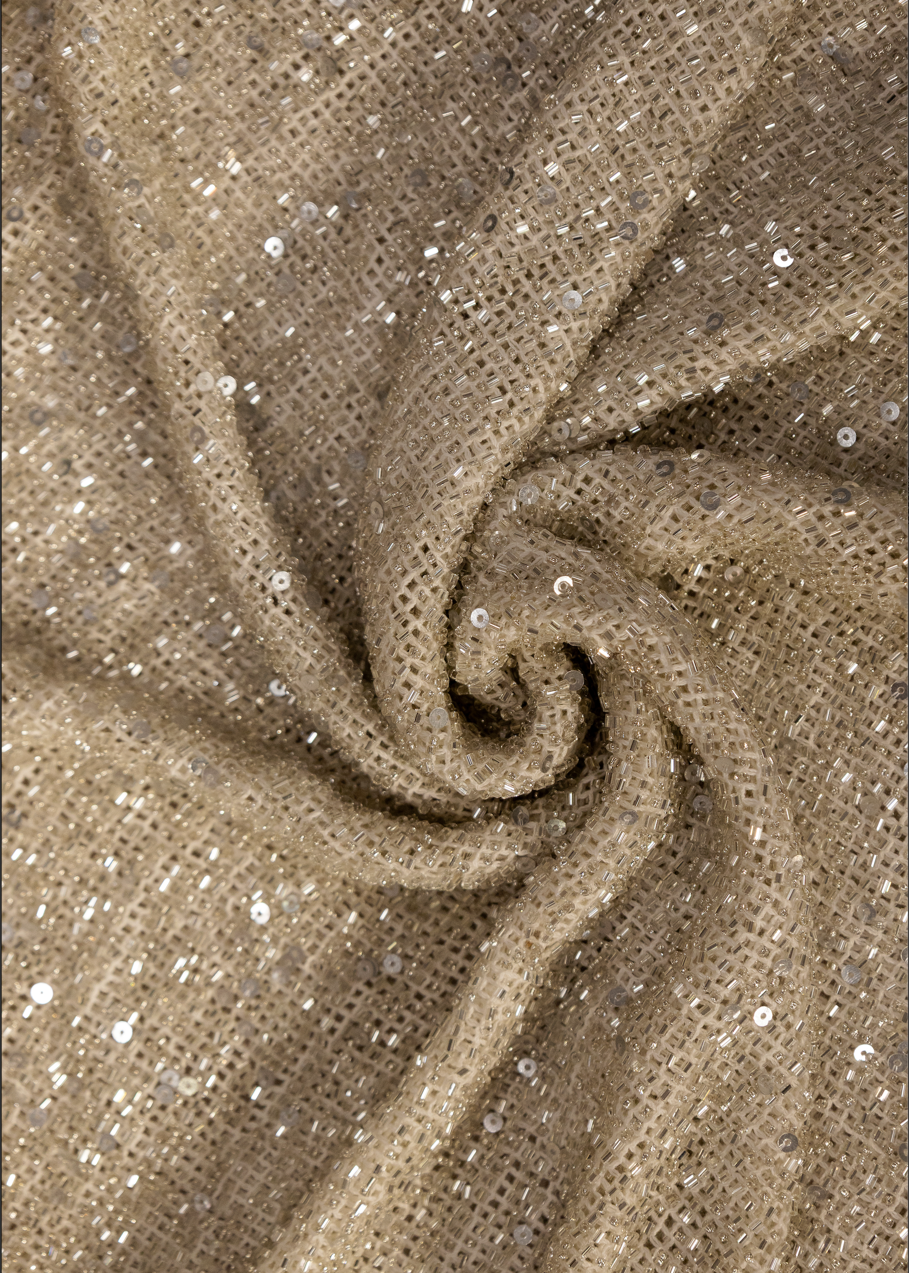 Detalle de tela beige con pedrería y lentejuelas sobre base de algodón texturizado