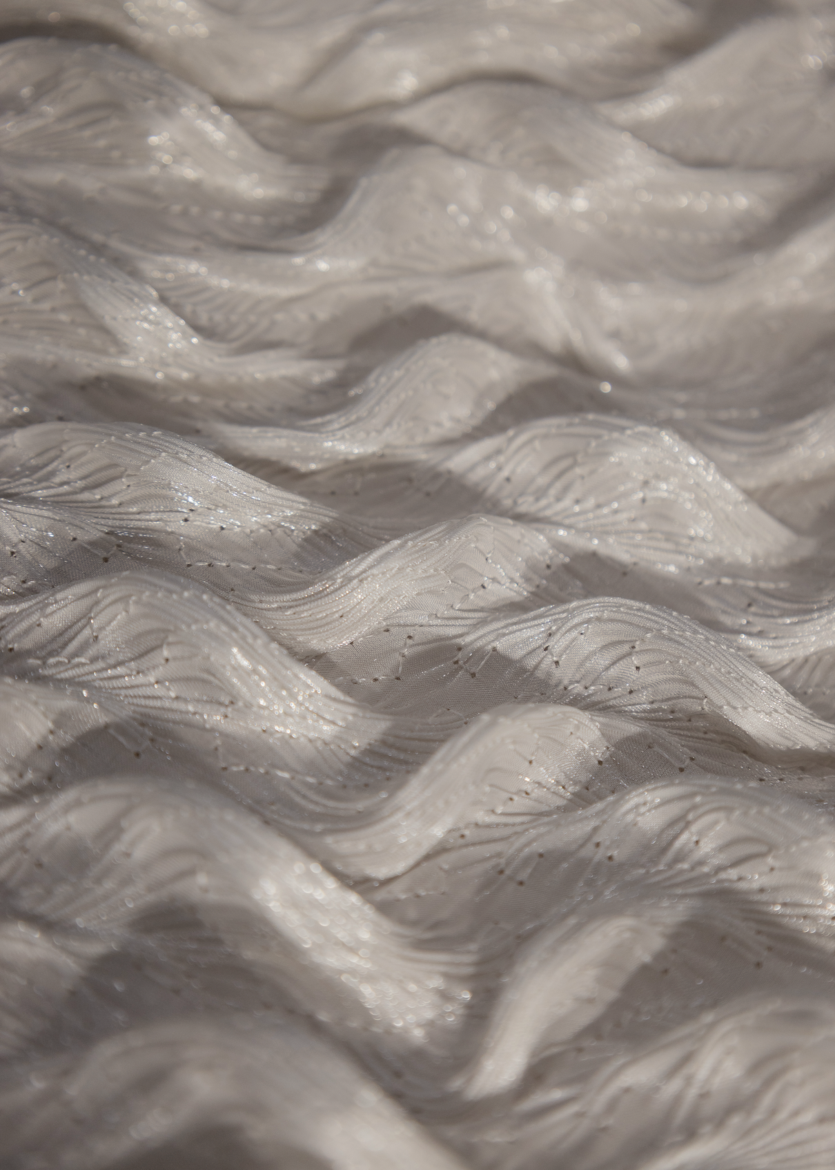 Detalle de tela blanca con textura ondulada en relieve y acabado perlado brillante