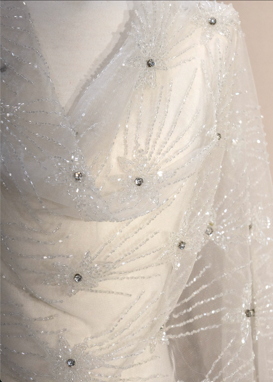 Detalle de bordado floral con pedrería y canutillo sobre tul, textura brillante y sofisticada.